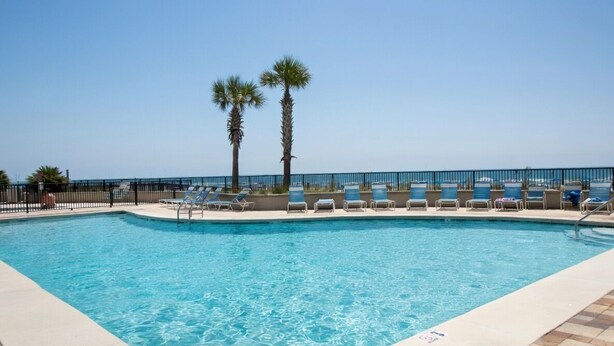 A swimming pool with lounge chairs and palm trees. - 14th Floor End Unit w/ Wraparound Balcony (Orange Beach)