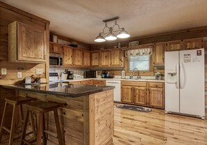 Una cocina con armarios de madera, una isla central con taburetes, un refrigerador y un microondas.