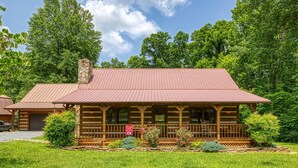 A rustic lodge with a prominent chimney, a covered porch, and a well-maintained lawn. - Cozy Two Bedroom Mountain Getaway - Log Cabin, One Story, Pet Friendly (Sevierville)
