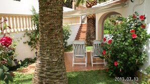 Ein Innenhof mit einer Palme, zwei weißen Stühlen und roten Blumen.