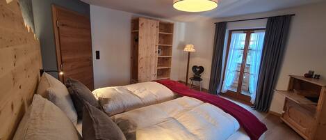 A bedroom with two beds, wooden headboard, a wardrobe, a bedside table, a lamp, and a window with curtains.