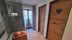 Une salle de bain moderne avec une douche en verre, un banc en bois avec des serviettes et une porte en bois ornée d’un motif en forme de cœur.
