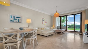 A spacious living room with a dining area, a sofa set, and a large sliding glass door leading to a garden.