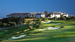 A golf course with bunkers and a large building with multiple chimneys in the background.