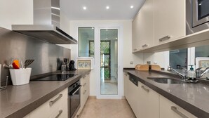 A modern kitchen with stainless steel appliances, a double sink, and a view through a glass door to a balcony.