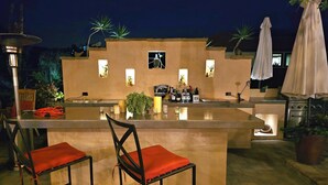 An outdoor bar area with a counter, two chairs, and a grill.