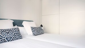 A neatly made bed with white linens and patterned pillows, a teal headboard, and a plain wall. - Muinoa 5 by FeelFree Rentals (San Sebastián)