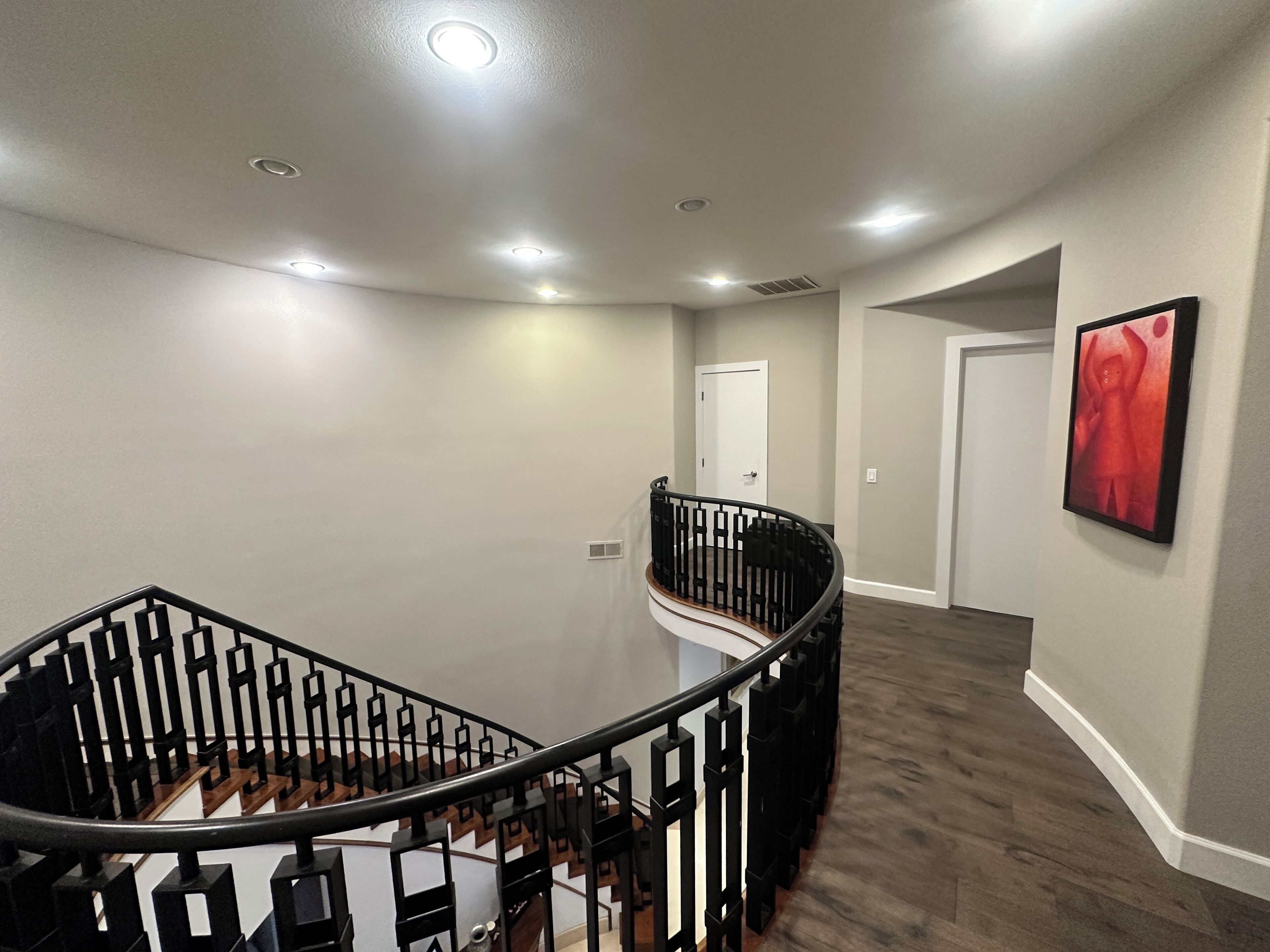 A modern interior with a spiral staircase, neutral walls, and a red abstract painting.