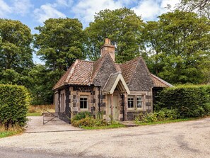 A stone cottage with a tiled roof, a chimney, and a gravel driveway.
