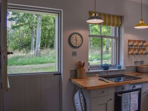 A kitchen with a window, a clock, a stove, and a sink.