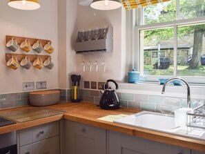 A modern kitchen with a wooden countertop, a kettle, a sink, and a window with a view of the outdoors.