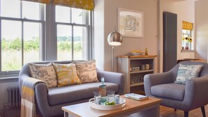 A living room with a sofa, armchair, and a coffee table with a tray of glasses and a book. - The Lodge @ East Neuk Orchards (Pittenweem, near Anstruther)