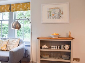A room with a sofa, a table with a bowl of fruit, a shelf with dishes, and a framed picture on the wall.