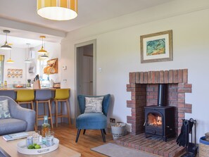 A cozy living room with a fireplace, a dining area with chairs, and a kitchen in the background.