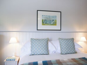 A neatly made bed with two pillows, a framed picture above, and two bedside lamps.