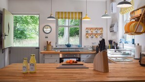 A modern kitchen with wooden countertops, hanging pendant lights, a window with a view of greenery, and a clock on the wall. - The Lodge @ East Neuk Orchards (Pittenweem, near Anstruther)