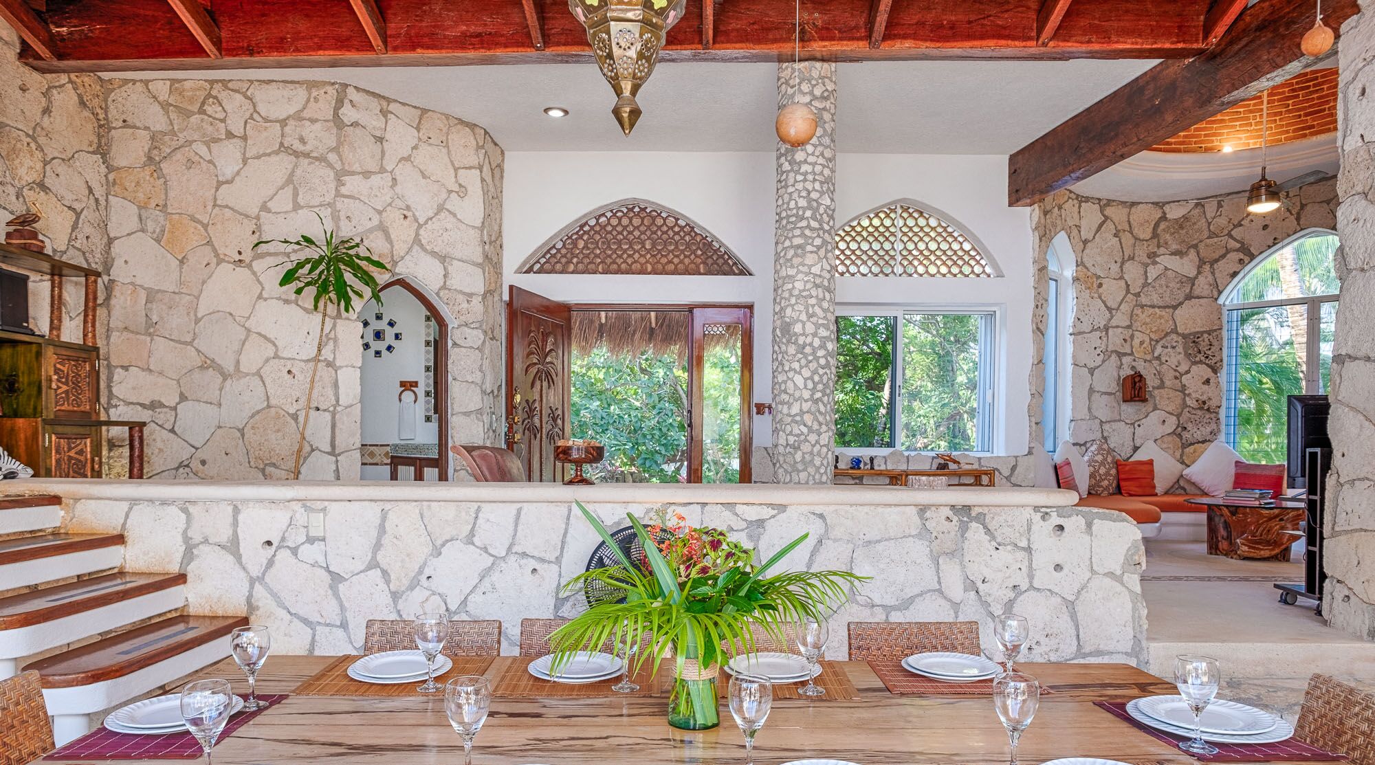 A dining area with stone walls, a wooden staircase, and a view of greenery outside.