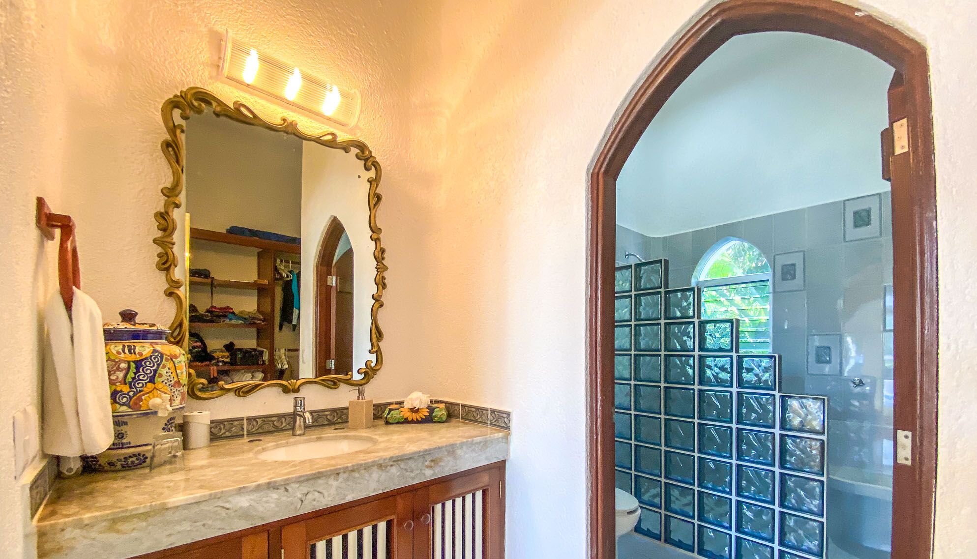 A bathroom with a marble sink, ornate mirror, and a view of a tiled shower area.