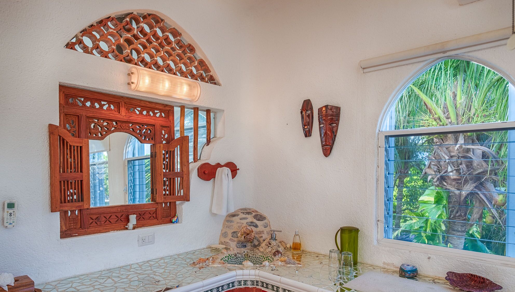 A bathroom with a decorative mirror, a stone sink, a window with a view of greenery, and a towel hanging on the wall.