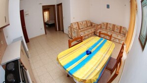 Un comedor con una mesa cubierta con un mantel a rayas, un sofá con cojines estampados, y una zona de cocina con estufa.