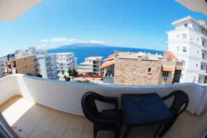 A balcony with two chairs and a table, overlooking a coastal cityscape with buildings and a clear blue sky. - Eleana Apartments (Sarandë)