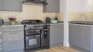 A modern kitchen with grey cabinets, a black stove, and a tiled backsplash. - 5 bedroom accommodation in Wimborne (Wimborne)