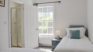 A bedroom with a bed, a nightstand, a window, and a door leading to a bathroom. - 5 bedroom accommodation in Wimborne (Wimborne)