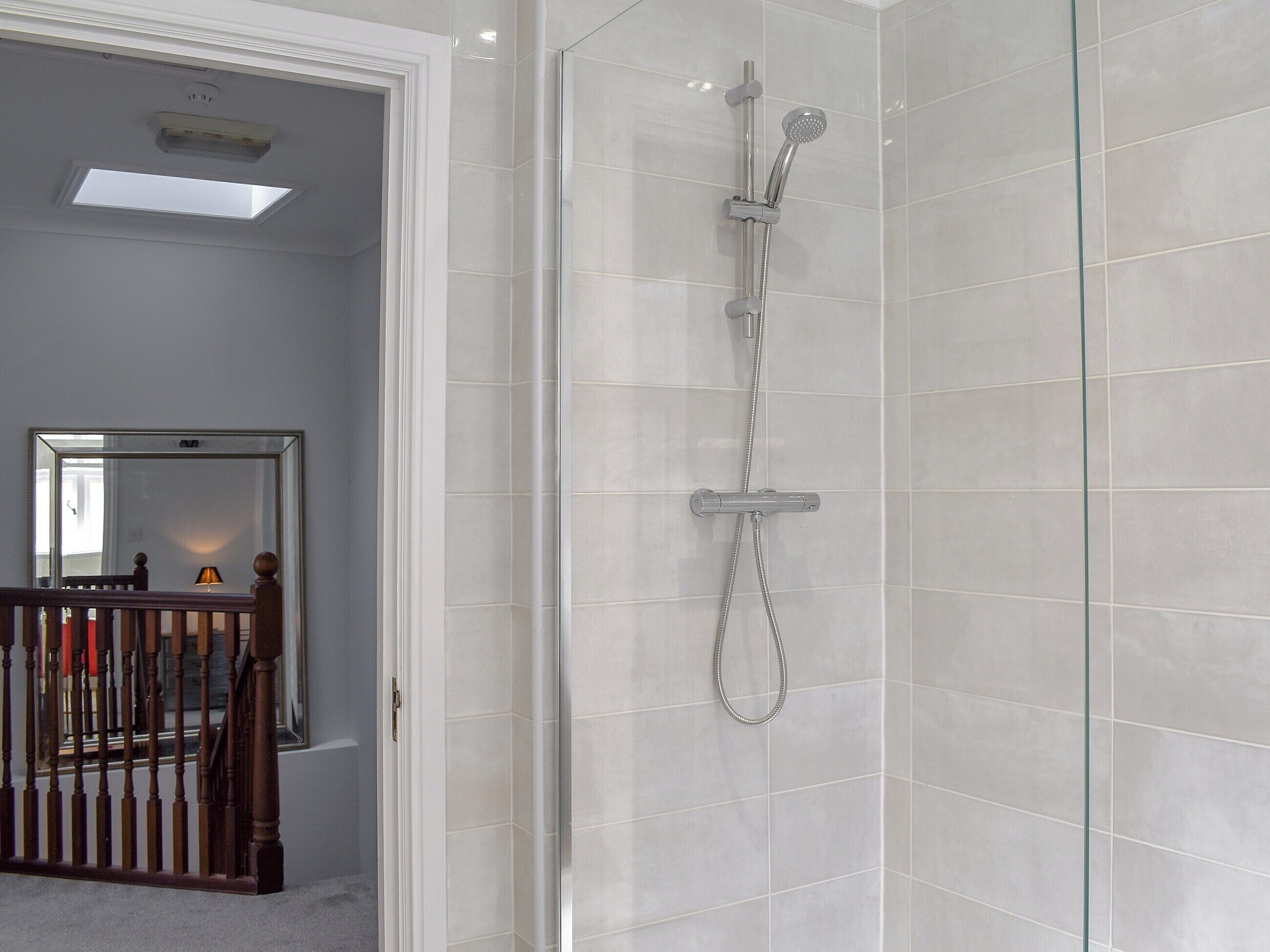 A modern bathroom with a glass shower enclosure, white tiled walls, and a wooden door.