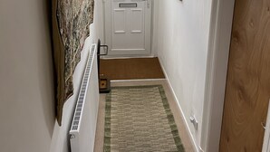 Un couloir avec une porte blanche, un radiateur, un paillasson marron et un tapis vert.