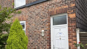 Une maison en briques avec une porte blanche, une petite fenêtre et une boîte aux lettres.