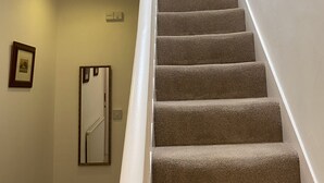Un escalier recouvert de moquette, avec des murs blancs et un tableau encadré accroché au mur.