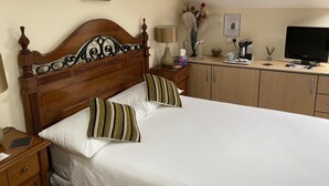 Un lit bien fait, agrémenté d’oreillers à rayures, une tête de lit en bois, une table de chevet avec une lampe, une petite armoire et un téléviseur posé sur un bureau.