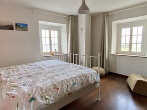 A bedroom with a single bed, two windows, a ceiling fan, and a woven bench. - Lovely home with ocean views just a 5 minute walk to stunning beaches! (Céltigos)