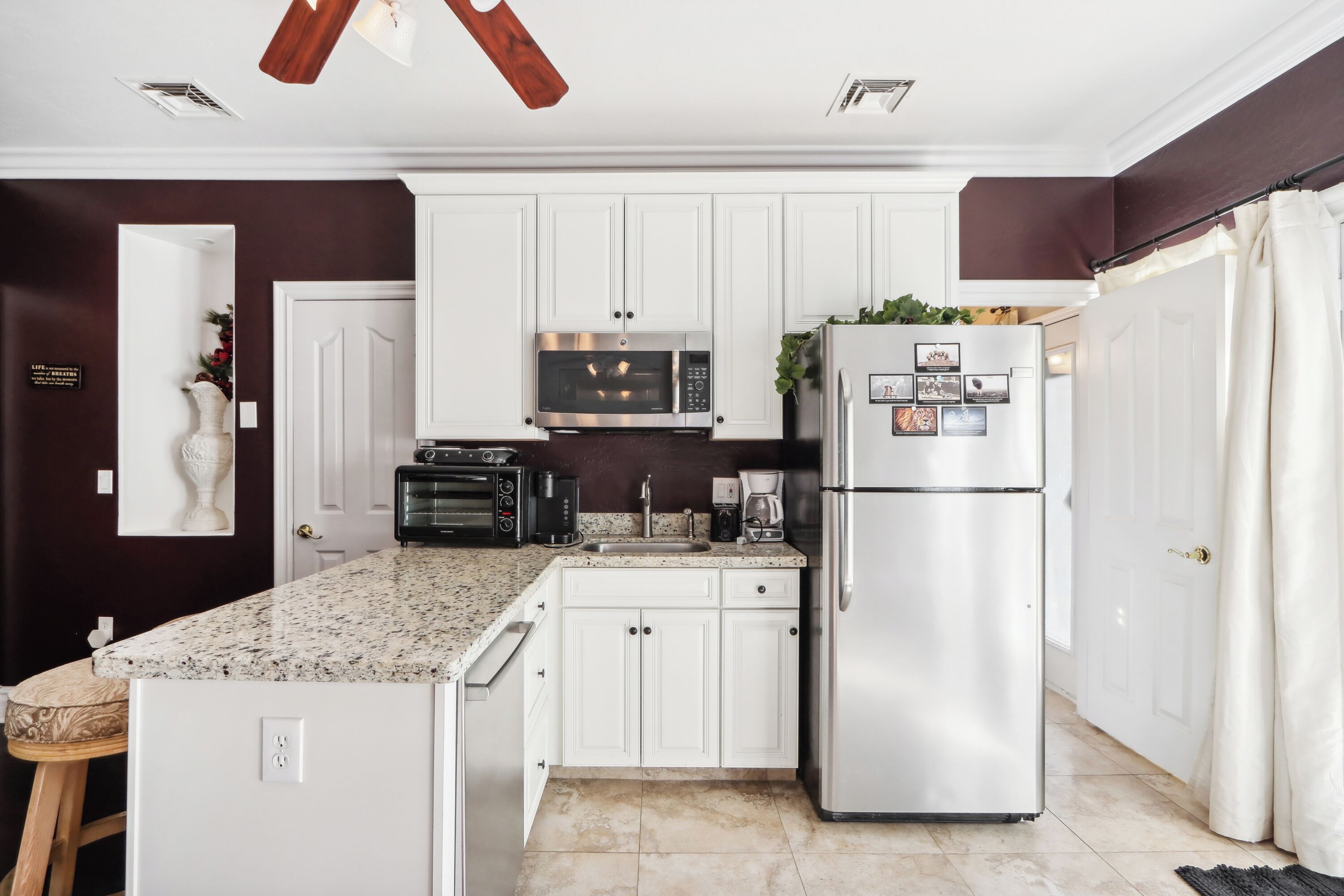 A modern kitchen with white cabinets, a stainless steel refrigerator, a microwave, and a built-in oven.