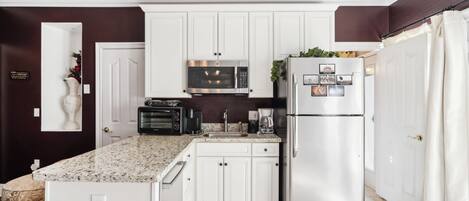 A modern kitchen with white cabinets, a stainless steel refrigerator, a microwave, and a built-in oven.