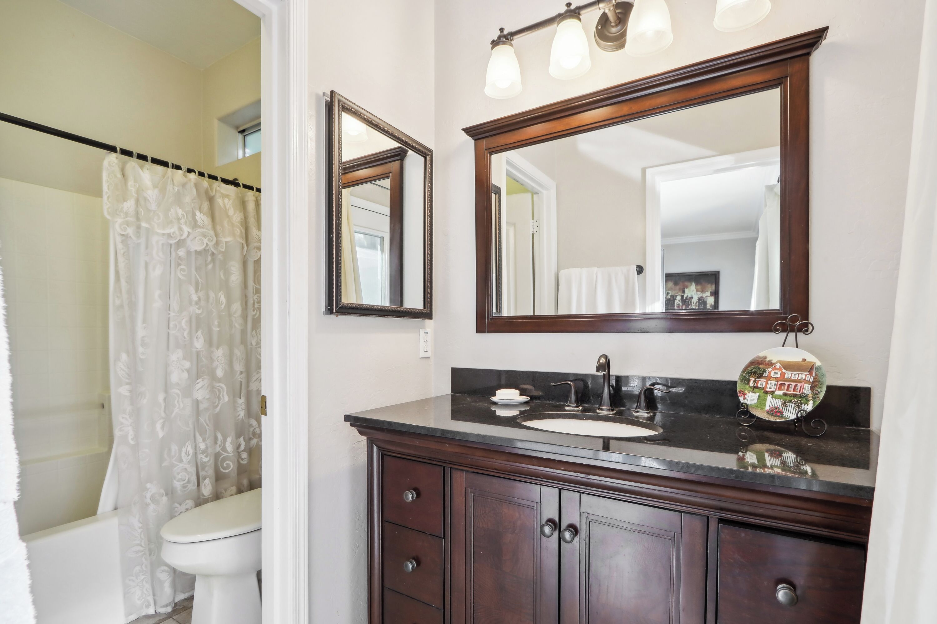 A bathroom with a white toilet, a dark wooden vanity with a sink, and two mirrors.