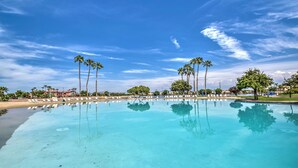 Ein klares, blaues Schwimmbecken mit Palmen und einem Gebäude im Hintergrund.