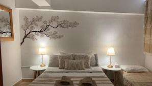 Una habitación de hotel con una cama, dos mesitas de noche, una lámpara de pared y un mural decorativo con un árbol.