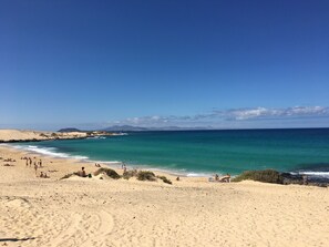Ein Strand mit klarem türkisblauem Wasser, Sanddünen und einigen Menschen, die die Aussicht genießen.