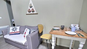 Een woonkamer met een grijze bank, een houten eettafel en een gele stoel.