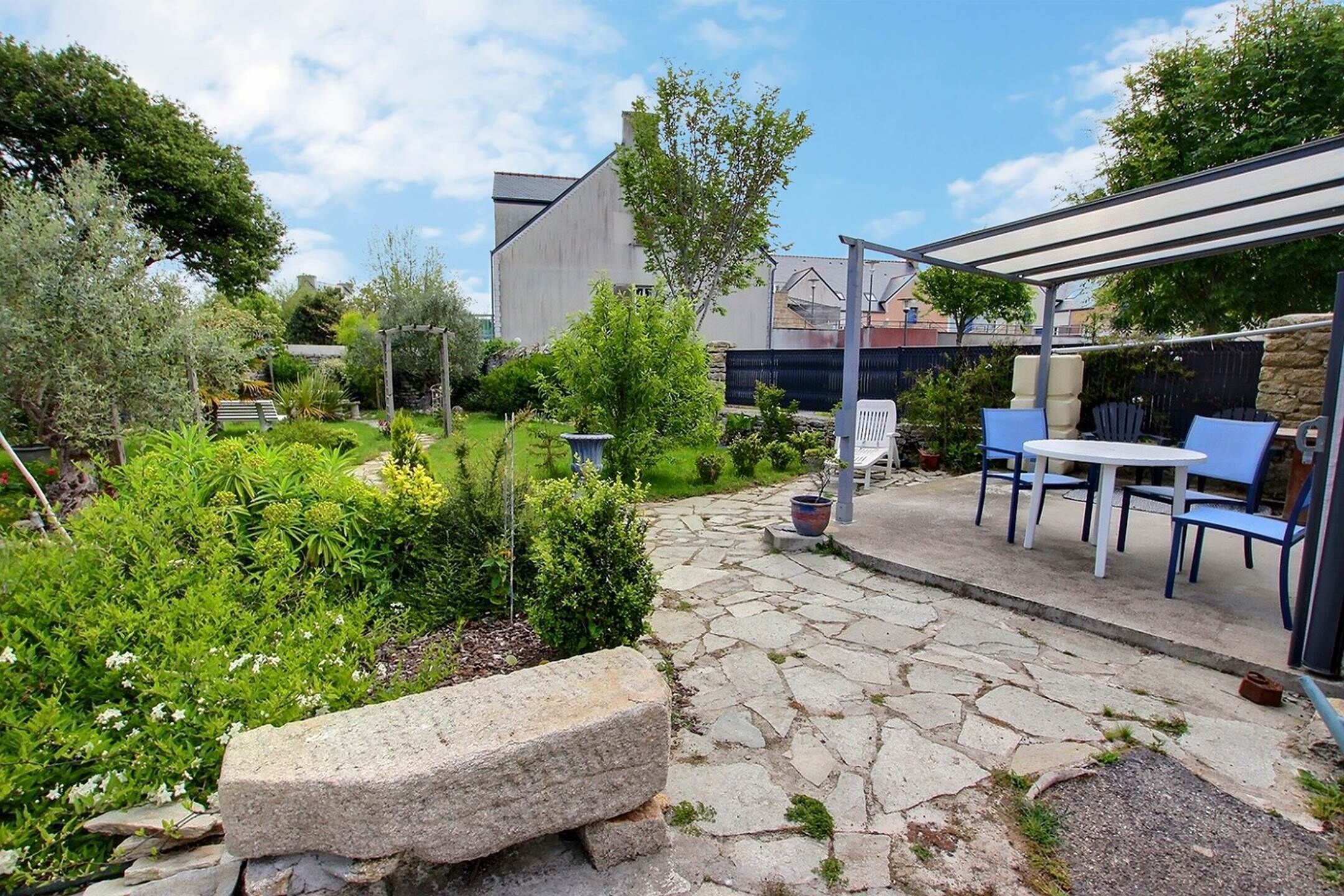 Een terras met stenen vloer, een stenen bank en blauwe tuinmeubels.