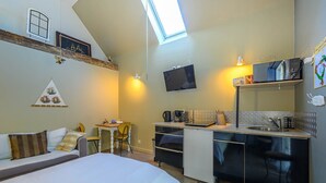 Een kleine kamer met een bed, bureau, kitchenette en televisie.