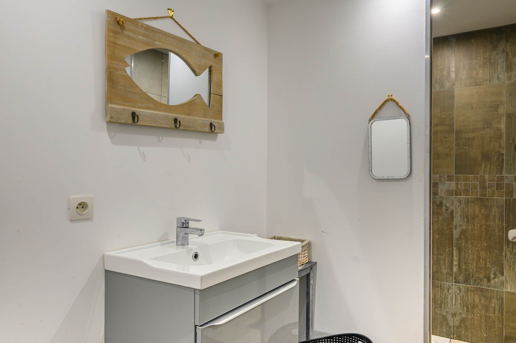 A bathroom with a white sink, a wooden-framed mirror, and a small mirror on the wall.