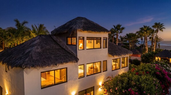 A two-story building with thatched roofs, multiple windows, and a view of the ocean.