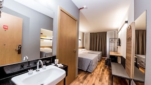 A modern hotel room with a wooden floor, a large mirror, a white sink, a bedside table, and a bed with a checkered bedspread. - Hotel 10 Balsas (Balsas)