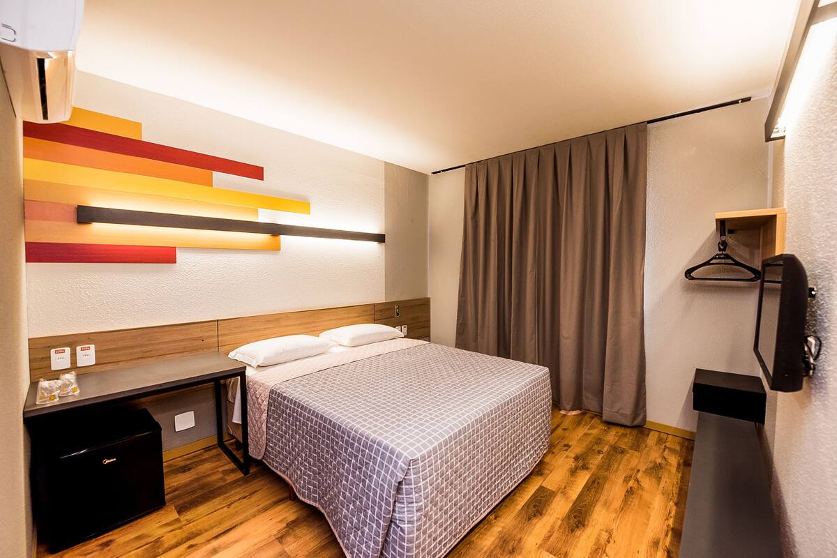 A hotel room with a bed, bedside table, and a wall-mounted light fixture.
