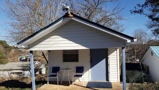 A small, single-story building with a covered porch, two chairs, and a table.