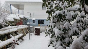 A snow-covered outdoor area with a house, a fence, and a trash can.