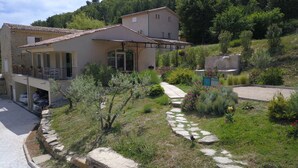 A two-story house with a tiled roof, a stone pathway leading to the entrance, and a garden with various plants and flowers. - Completely renovated Mas Provencal (Manosque)