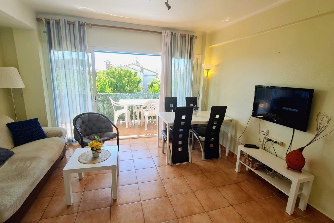 A living room with a sofa, a coffee table with a vase, a TV, a dining table with chairs, and a balcony with a view.